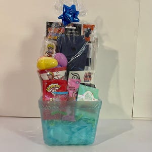 May include: A gift basket filled with various items, including candy, a leg pouch, and toys. The basket is wrapped in clear cellophane and topped with a blue bow. The basket itself is a clear, glittery container with blue and red accents.