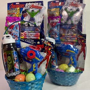 May include: Two blue woven Easter baskets filled with Avengers-themed toys and candy. Each basket contains a water bottle, a toy blaster, and colorful eggs. Packages of Haribo Goldbears, Skittles, and other treats are also included.