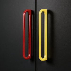 May include: Close-up of a black cabinet door with two colorful handles. One handle is bright red, and the other is yellow. The handles are a curved, elongated design.
