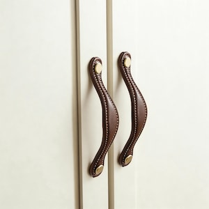 May include: A white ceramic mug with a black handle and the text "But First, Coffee" in a black, bold font. The mug is on a white surface.