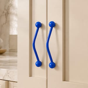May include: Two bright blue cabinet handles with a curved, wave-like shape and spherical ends. The handles are mounted vertically on light beige cabinet doors, featuring a smooth, glossy finish that contrasts with the neutral cabinetry.