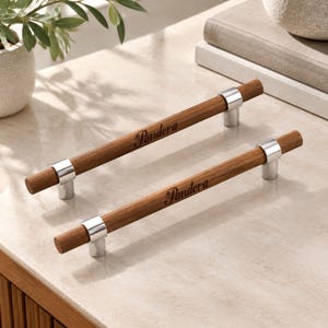Peut inclure: Deux poignées de placard cylindriques avec une finition en bois brun moyen et des supports de montage en métal argenté poli. Chaque poignée est gravée du mot Pandora dans une police cursive, centré le long de la barre en bois.