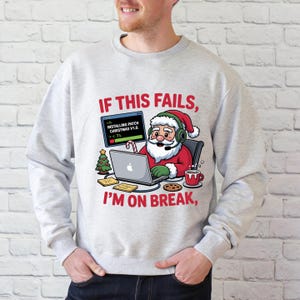 May include: Light gray sweatshirt with a graphic of Santa Claus wearing a headset and working on a laptop. The text reads "IF THIS FAILS, I'M ON BREAK." Santa is surrounded by Christmas-themed icons, including a tree and a candy cane.