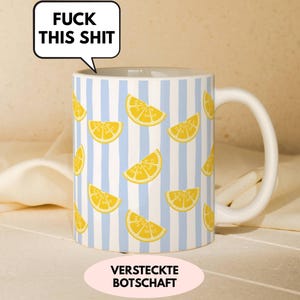 Könnte beinhalten: Ein weißer Keramikbecher mit einem Muster aus gelben Zitronenscheiben auf hellblauen vertikalen Streifen. Eine Sprechblase am oberen Rand enthält den Text FUCK THIS SHIT in schwarzen Großbuchstaben. Der Becher hat einen geschwungenen Henkel.