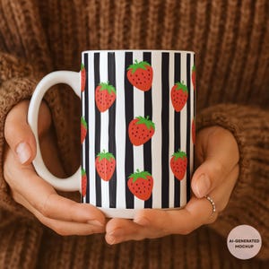 May include: A white ceramic mug featuring a repeating pattern of red strawberries with green leaves against a background of vertical black stripes. The mug has a curved handle on the left side and a smooth, cylindrical body with a glossy finish.