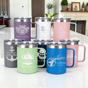 Puede incluir: Una colección de tazas de viaje aisladas en varios colores, incluyendo morado, blanco, rosa, gris, verde, azul y rosa. Cada taza tiene una tapa plateada, un asa y grabados personalizados con texto y diseños. Las tazas miden aproximadamente 13 cm de alto.