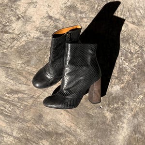 May include: A pair of black ankle boots with a snakeskin pattern. The boots have a zipper closure and a wooden block heel. The boots are approximately 4 inches tall.