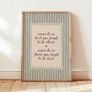Può includere: Una stampa rettangolare incorniciata con un pannello centrale beige chiaro dal bordo smerlato, circondato da uno sfondo a righe verticali verde salvia e bianco. Il testo recita: never be so kind you forget to be clever, never be so clever you forget to be kind.