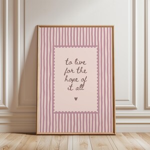 May include: A framed vertical wall art print featuring a light pink background with dark pink vertical stripes. In the center, a scalloped-edge rectangle contains the dark brown text "to live for the hope of it all" and a small heart symbol.