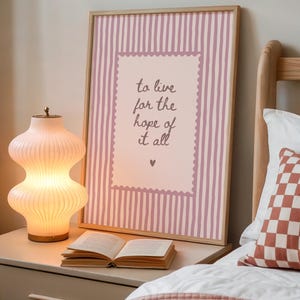 May include: A framed wall art print featuring a light pink and white vertical striped background with a central scalloped-edge rectangle containing the dark brown handwritten text: to live for the hope of it all, finished with a small heart icon.