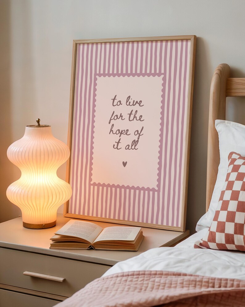 May include: A framed wall art print featuring a light pink and white vertical striped background with a central scalloped-edge rectangle containing the dark brown handwritten text: to live for the hope of it all, finished with a small heart icon.