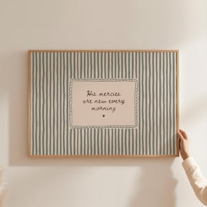 Può includere: Un quadro rettangolare con cornice in legno chiaro caratterizzato da un motivo a righe verticali color verde salvia tenue e crema. Al centro, un riquadro color crema con bordo smerlato riporta la scritta His mercies are new every morning e un piccolo cuore.