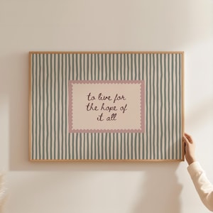 May include: A rectangular wall art print in a light wood frame featuring a vertical striped pattern in muted green and cream. Centered is a rectangular cream-colored label with a scalloped pink border containing the text to live for the hope of it all.