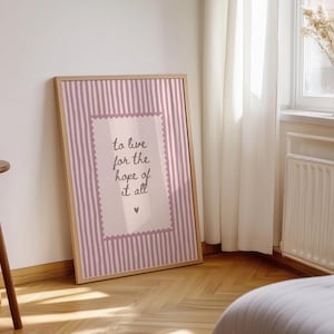 May include: A framed rectangular wall art print featuring a light pink and white vertical striped background. A central rectangular panel with a scalloped border contains the dark text: to live for the hope of it all, with a small heart below.