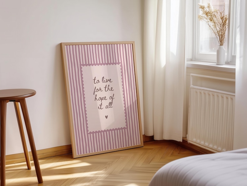 May include: A framed rectangular wall art print featuring a light pink and white vertical striped background. A central rectangular panel with a scalloped border contains the dark text: to live for the hope of it all, with a small heart below.