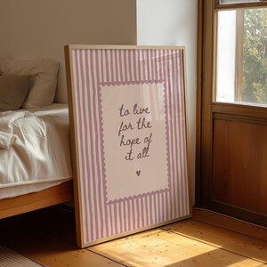May include: A rectangular framed wall art print featuring a light pink background with vertical white stripes. In the center, a scalloped-edge rectangle contains the dark text 'to live for the hope of it all' and a small heart symbol below.
