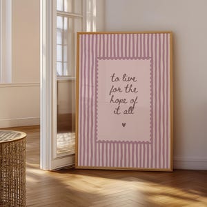 May include: A rectangular framed wall art piece featuring a light pink background with vertical dark pink stripes. A central light pink rectangle with a scalloped border contains the dark text: to live for the hope of it all, with a small heart below.