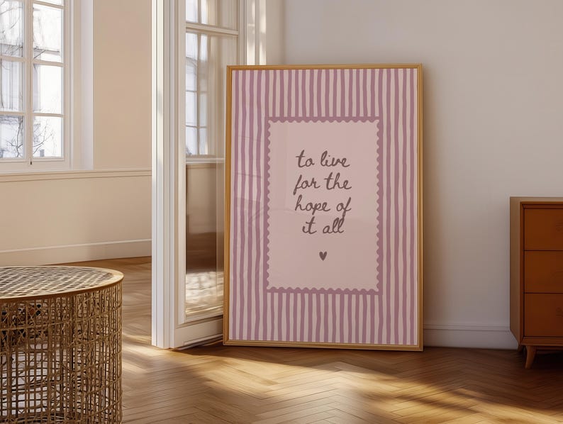 May include: A rectangular framed wall art piece featuring a light pink background with vertical dark pink stripes. A central light pink rectangle with a scalloped border contains the dark text: to live for the hope of it all, with a small heart below.