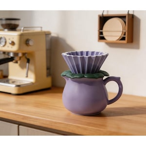 Puede incluir: Un juego de cerámica morada para verter café con una base en forma de flor y un soporte de filtro plisado. El juego está sobre una superficie de madera, con una máquina de espresso amarilla al fondo. Un soporte de madera con filtros de café cuelga de la pared.