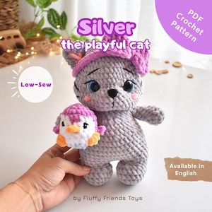 Può includere: Un giocattolo a forma di gatto grigio all'uncinetto con un fiocco rosa e un piccolo giocattolo a forma di pinguino. Il gatto ha gli occhi blu e tiene in mano il pinguino. Il testo sull'immagine recita "Silver the playful cat" e "Low-Sew". Il modello è disponibile in inglese.