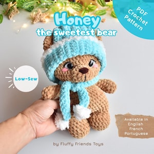 Op de afbeelding: Een gehaakte teddybeer genaamd "Honey" met een lichtblauwe muts en sjaal met witte accenten. De beer heeft een bruin lichaam, een bruine neus en roze wangen. De afbeelding bevat de tekst "PDF Crochet Pattern" en "Low-Sew".