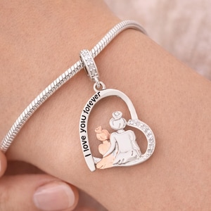 以下が含まれることがあります： ハート型のペンダントが付いたシルバーチャームブレスレット。ペンダントには、母親と子供のデザインと「I love you forever」の文字が施されています。ハートはクリアクリスタルで装飾されています。