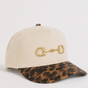 May include: A cream-colored snapback hat with a cheetah print brim and a gold-colored horse bit design. The text "Horse Bit Cheetah" is above the hat, and "Rosewood Ranch Co." is below.