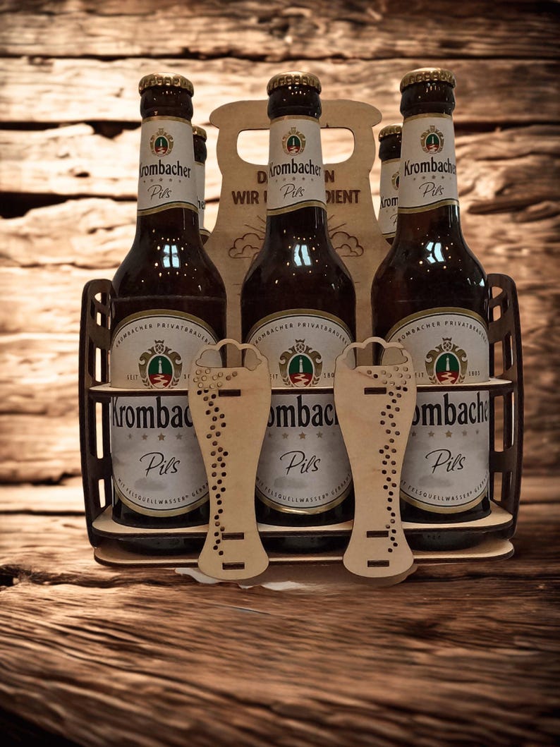 May include: A wooden beer carrier holding six bottles of Krombacher Pils beer. The bottles are brown with gold caps and white labels. Two wooden beer glass cutouts are in front of the bottles. The carrier has the text "D WIR N DIENT".
