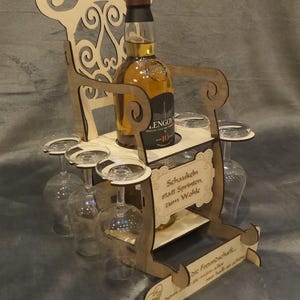 May include: A wooden wine bottle and glass holder in the shape of a chair. The holder has a bottle of liquor and several wine glasses. The chair has decorative cutouts and text on the front. The wood is light brown.