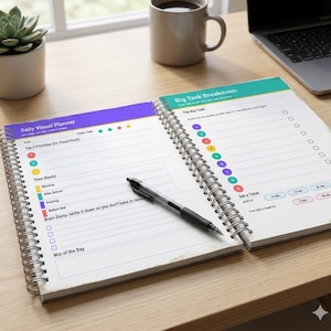 May include: A spiral-bound daily visual planner open to two pages with a black pen resting on the left side. The left page features sections for priorities, time blocks, and a brain dump. The right page includes a big task breakdown section.