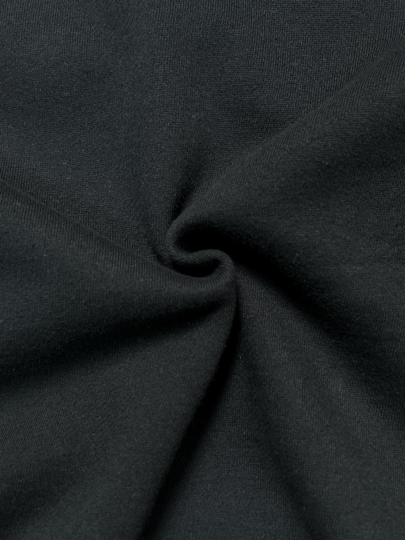 Puede incluir: Primer plano de tela negra con textura y pliegues visibles. El material parece suave y opaco, con sutiles variaciones de tono. La imagen resalta la textura y la ca&iacute;da del tejido.