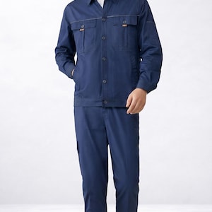 May include: Navy blue work uniform set. The set includes a collared jacket with two chest pockets and matching pants. The jacket has button closures and orange stitching details. The person is wearing white sneakers.