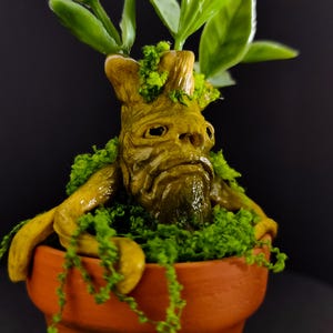 Op de afbeelding: Handgemaakte sculptuur van een Alruinplant in een terracotta pot. De plant heeft een gedetailleerd, expressief gezicht met groen mos en bladeren. Een uniek stuk voor interieurdecoratie.