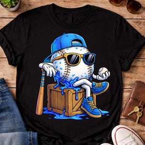 Può includere: T-shirt nera con un personaggio di baseball dei cartoni animati con occhiali da sole e un berretto blu, seduto su una cassa di legno. La palla da baseball tiene una mazza e una palla, con dettagli blu.
