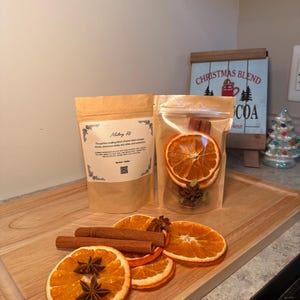 May include: A wooden board displays a mulling kit with dried orange slices, star anise, and cinnamon sticks. A clear bag contains similar ingredients. A sign reads "Christmas Blend Cocoa Here."