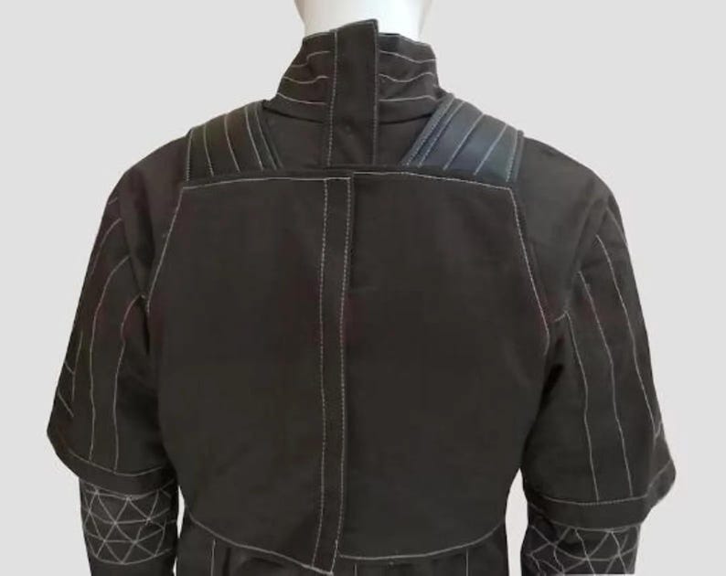 K&ouml;nnte beinhalten: Schwarze Jacke mit wei&szlig;en N&auml;hten. Die Jacke hat einen hohen Kragen, gepolsterte Schultern und geometrische Muster an den &Auml;rmeln. Die R&uuml;ckansicht zeigt die N&auml;hte und Designdetails des Kleidungsst&uuml;cks.