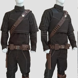 K&ouml;nnte beinhalten: Zwei schwarze Kost&uuml;me mit braunen Akzenten werden auf Schaufensterpuppen pr&auml;sentiert. Jedes Outfit umfasst ein Oberteil mit hohem Kragen, eine Hose, einen G&uuml;rtel mit Taschen und einen Schulterriemen. Die Kost&uuml;me haben wei&szlig;e N&auml;hte und braune Holster.