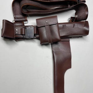 K&ouml;nnte beinhalten: Ein brauner Leder-Utility-G&uuml;rtel mit mehreren Taschen, einer Halterung und Schlaufen zur Aufnahme von Gegenst&auml;nden. Der G&uuml;rtel hat eine silberfarbene Schnalle und ist f&uuml;r das Tragen von Zubeh&ouml;r konzipiert.