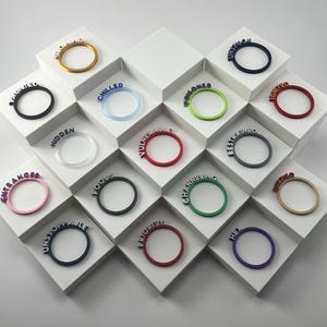 May include: A collection of colorful rings, each with a word attached. The rings are displayed on white geometric platforms. Colors include black, blue, red, green, pink, and gold. The words include "Focused", "Chilled", "Unstoppable", and more.