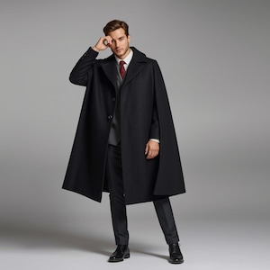May include: A black wool cape coat with a classic design. The coat features a button-down front, a wide collar, and a tailored fit. The model is wearing a white shirt, a gray vest, a red tie, and black dress pants.