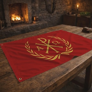 May include: A red flag with a gold emblem featuring the Chi-Rho symbol, a wreath, and the letters Alpha and Omega. The flag is displayed on a wooden table.
