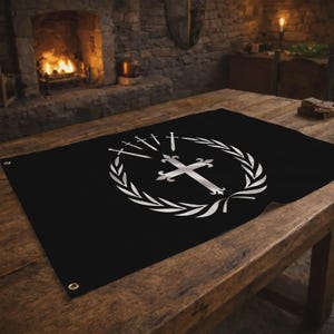 Può includere: Bandiera nera con un emblema argentato raffigurante una croce, spade e una corona d'alloro. La bandiera è rettangolare con occhielli agli angoli. La bandiera è esposta su un tavolo di legno.