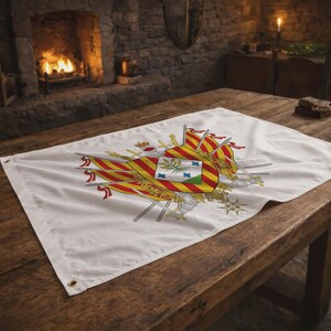 Könnte beinhalten: Weißes Banner mit einem detaillierten Emblem in Rot, Gelb und Grün. Das Emblem zeigt Flaggen, eine Krone und heraldische Elemente. Das Banner liegt auf einem Holztisch in einem Raum mit Kamin.