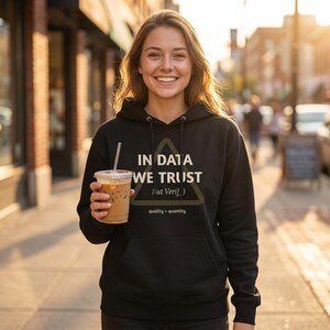 Puede incluir: Sudadera con capucha negra con el texto "IN DATA WE TRUST (But Verify)" en blanco y un diseño de triángulo. La sudadera también tiene el texto "quality > quantity" debajo del triángulo. La persona sostiene un vaso de plástico transparente con café helado.