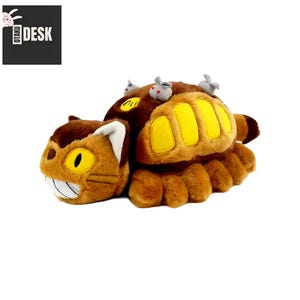 Puede incluir: Un peluche marr&oacute;n con forma de criatura felina, con detalles amarillos y una cara sonriente. Peque&ntilde;as figuras grises con forma de rat&oacute;n est&aacute;n en la espalda. El logotipo "OTAKU DESK" es visible en la esquina superior izquierda.