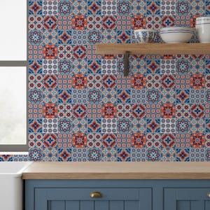 Puede incluir: Un salpicadero de cocina con un patrón repetitivo de azulejos azules, naranjas y blancos. Los azulejos tienen un diseño geométrico con motivos florales y estrellados. Una estantería de madera sostiene cuencos de cerámica blancos. Los armarios de abajo están pintados de azul.
