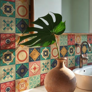 Może przedstawiać: Wnętrze łazienki z kolorową ścianą z płytek. Terakotowa waza zawiera duży zielony liść. Widoczna jest biała umywalka i kran, a także lustro.