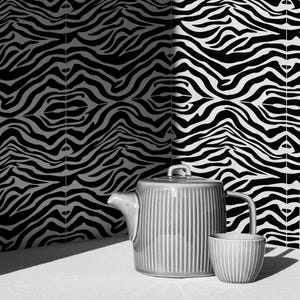 May include: A gray ceramic teapot and teacup set with vertical ribbed detailing. The background features a black and white zebra stripe pattern. The set is placed on a white surface, creating a minimalist aesthetic.