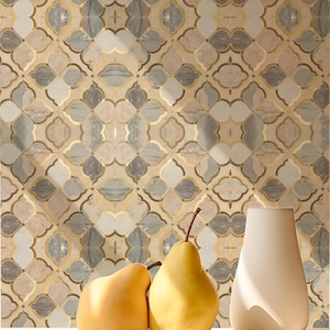 Pode incluir: Mosaico decorativo de parede com um padrão repetitivo de formas florais cinzentas, bege e douradas. Duas peras amarelas e um vaso branco em primeiro plano, criando uma composição de natureza morta.