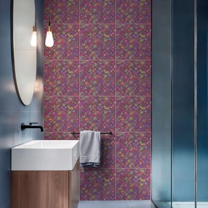 Op de afbeelding: Moderne badkamer met een geometrisch patroon op de muur en het plafond. De tegels hebben een kleurrijk abstract ontwerp in paars, groen en geel. Een witte wastafel met een houten kast en een zwarte kraan zijn zichtbaar.